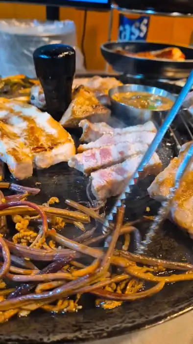 솥뚜껑 위에서 맛있게 익어가는 삼겹살과 꽈리고추, 콩나물