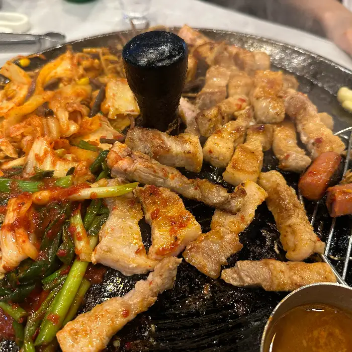 솥뚜껑 위에서 맛있게 익은 삼겹살과 김치, 콩나물, 파, 소시지