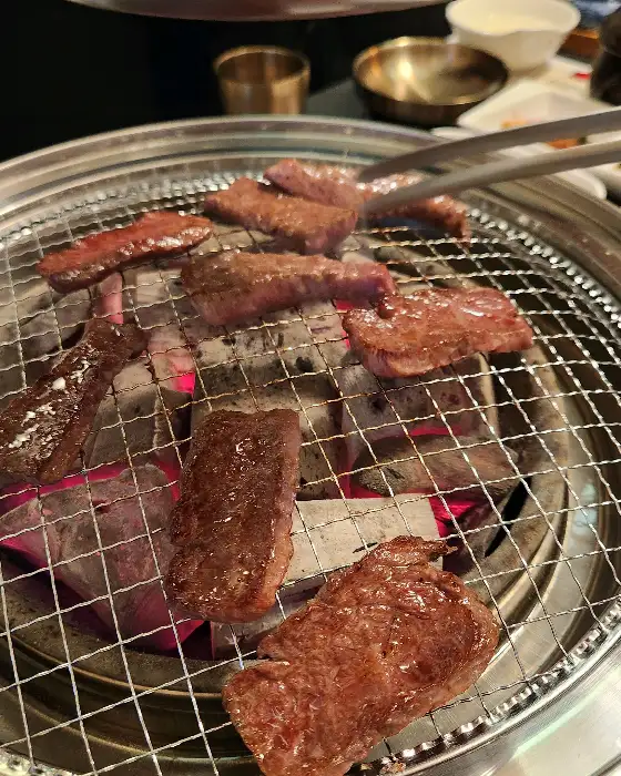 숯불 위에서 맛있게 구워지고 있는 한우 조각들. 붉은 숯불의 열기가 고기의 맛을 더해줄 것 같습니다.