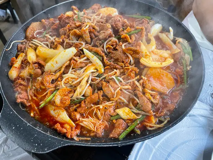 넓은 불판 위에서 오리 주물럭이 지글지글 익어가고 있습니다. 양파, 부추, 떡 등이 함께 어우러져 먹음직스럽습니다.
