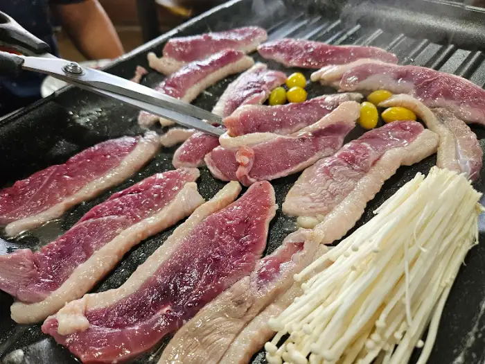 불판 위에서 오리고기가 노릇하게 익어가고 있습니다. 가위와 집게로 먹기 좋게 자르고 있습니다.