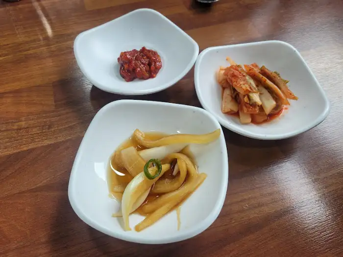 세 가지 밑반찬이 담긴 작은 그릇들. 김치, 깍두기, 양파 절임으로 보임.