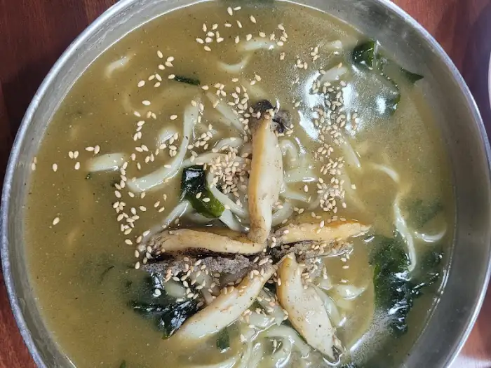 테이블 위에 놓인 전복 칼국수 그릇과 국물, 면발이 보임.