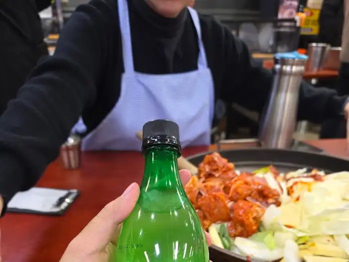 닭갈비 조리 중인 모습, 쇠 물병과 소주병이 보인다.