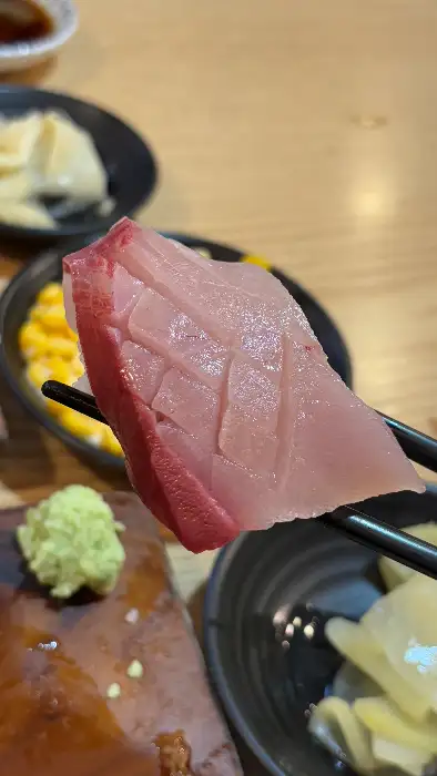 집게로 집어 올린 두툼한 활어회 조각