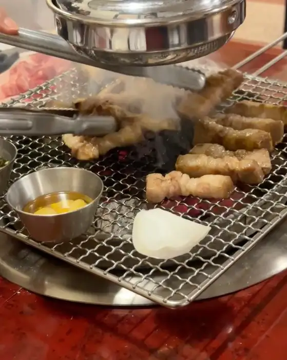 숯불 위에서 익어가고 있는 돼지고기와 곁들임 재료