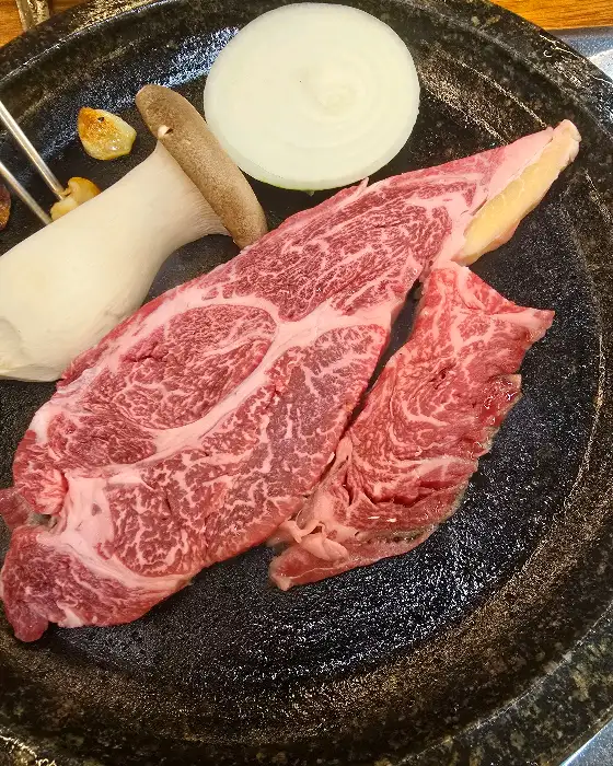 돌판 위에 올라간 두툼한 소고기 조각과 버섯, 양파가 먹음직스럽습니다.