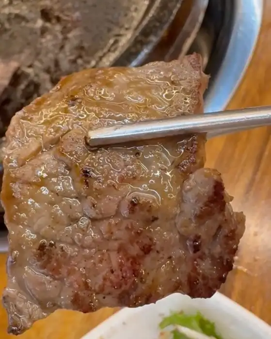 집게로 집힌 잘 구워진 소고기 조각이 육즙을 머금고 있습니다.