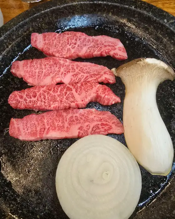 돌판 위에 구워지고 있는 두툼한 소고기 조각들과 버섯, 양파가 보입니다.