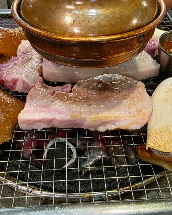 두툼한 삼겹살 한 점이 숯불 위에서 익고 있는 모습
