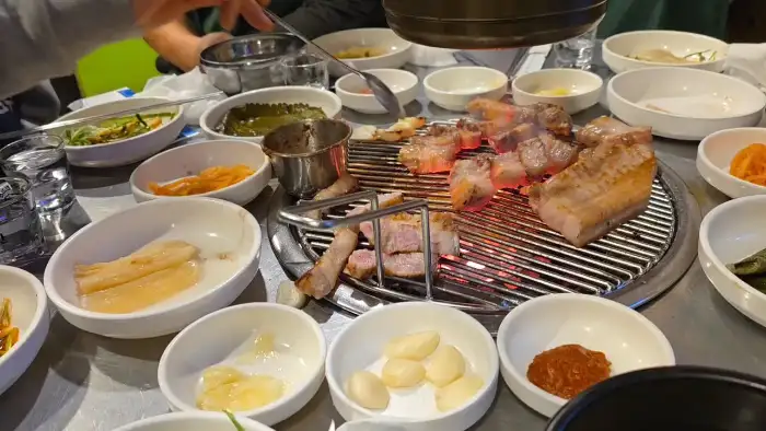테이블에 둘러앉아 연탄불에 구워지는 고기와 다양한 밑반찬들