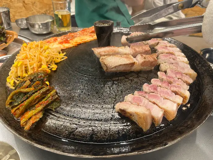 솥뚜껑 위에서 익어가는 삼겹살과 곁들임 찬들