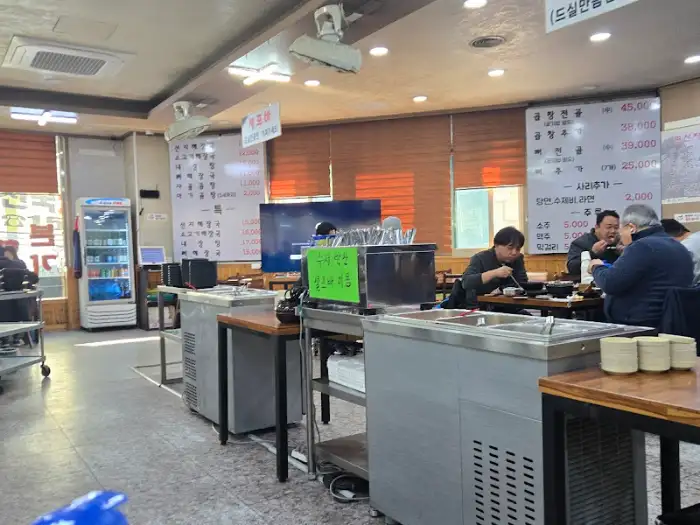 식당 내부의 모습. 테이블에는 사람들이 앉아 식사 중이며, 벽면에는 메뉴판이 붙어 있다.