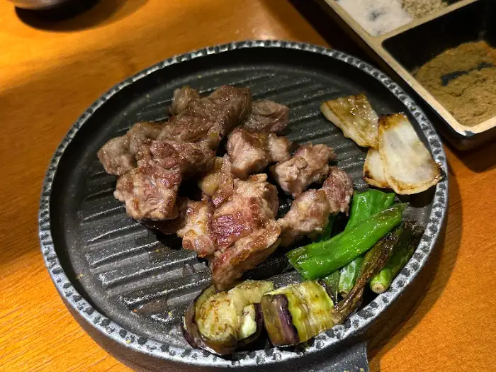 잘 구워진 양갈비 조각들이 접시에 담겨 있고, 곁들임 채소가 함께 놓여 있다.