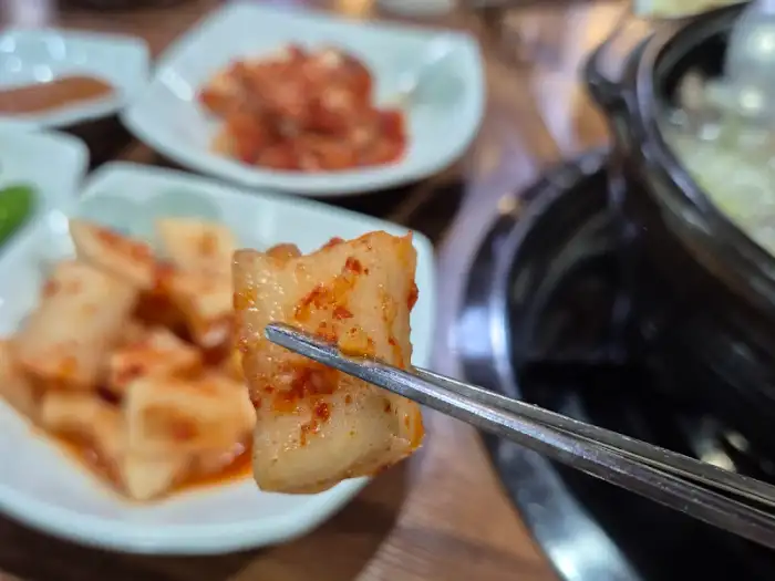 집게로 도가니와 김치를 함께 집어 올리고 있다.