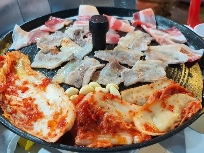 솥뚜껑 위에서 익어가는 삼겹살과 김치, 마늘