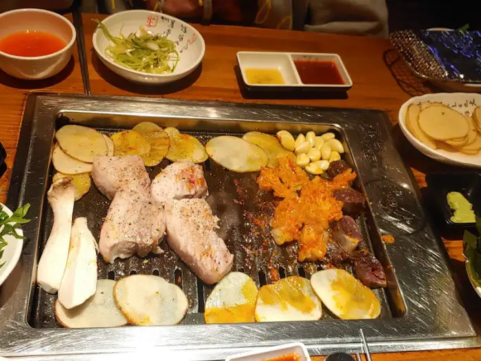 불판 위에 삼겹살, 대창, 감자슬라이스가 올라가 익고 있는 모습