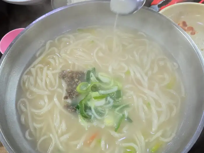 하얀 국물의 칼국수에 파와 다진 고명이 올라간 모습