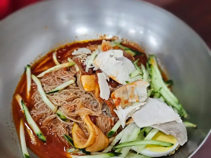 비빔 밀면에 올려진 편육 조각과 오이채