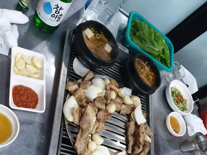 구워지고 있는 삼겹살과 곁들임 메뉴들. 불판 위에 고기와 마늘, 양파가 익어가고 있다.