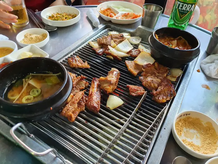 테이블 위에 푸짐하게 차려진 구이 메뉴와 곁들임 반찬. 다양한 고기와 채소가 불판 위에서 익어가고 있다.