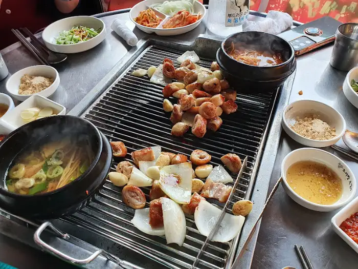 막창 구이와 곁들임 채소, 국물이 담긴 뚝배기가 보인다.