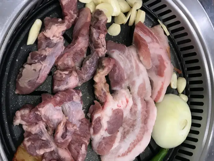 불판 위에 돼지고기와 마늘, 양파 조각들이 올라가 구워지고 있습니다.