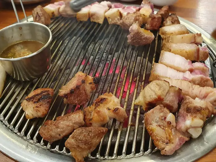 숯불 위에서 노릇하게 익어가고 있는 삼겹살 조각들. 붉은 숯불이 고기 익는 소리와 함께 시각적인 즐거움을 더합니다.