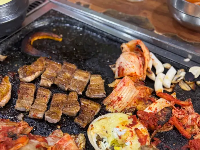 돌판 위에서 익어가는 삼겹살과 김치, 떡의 모습