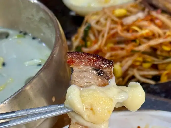 집게로 집은 삼겹살 조각이 치즈에 녹아내리고 있는 모습