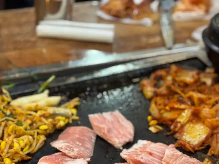 돌판 위에 놓인 썰어져 있는 생고기 조각들과 김치, 콩나물무침