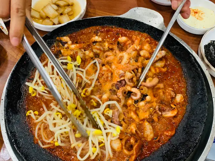 쭈꾸미를 콩나물과 함께 집어드는 집게. 붉은 양념이 묻어 먹음직스럽다.