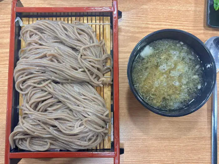 식사 테이블 위, 2단으로 쌓인 메밀면과 곁들임 육수 그릇. 메밀면의 윤기와 색감이 돋보인다.