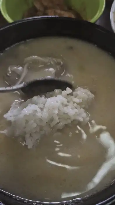 숟가락으로 밥을 국물에 푸는 모습. 밥알이 국물에 섞이며 먹음직스러워 보인다.