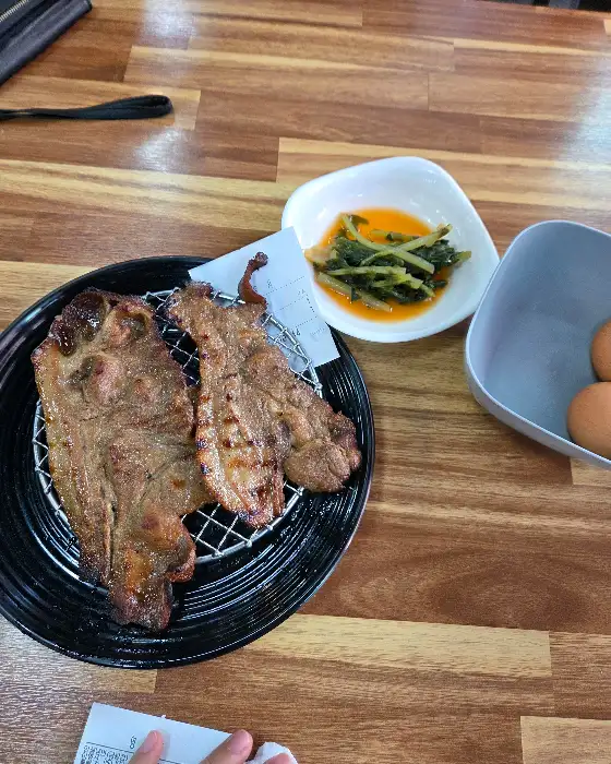 넓은 나무 테이블 위에 놓인 숯불고기 접시, 열무김치, 그리고 삶은 계란