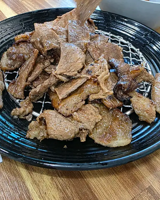 금빛으로 구워진 숯불고기가 빼곡하게 담긴 검은색 철망 접시