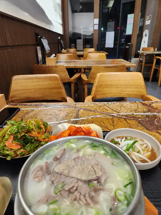 나무 테이블 위로 설렁탕과 겉절이, 깍두기, 그리고 숭늉이 담긴 그릇들이 놓여있는 모습