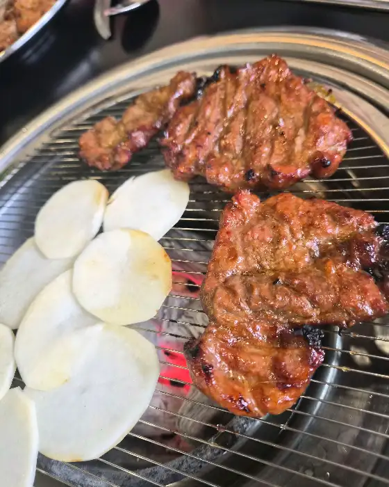 숯불 위에서 맛있게 익어가는 돼지갈비와 얇게 썬 감자