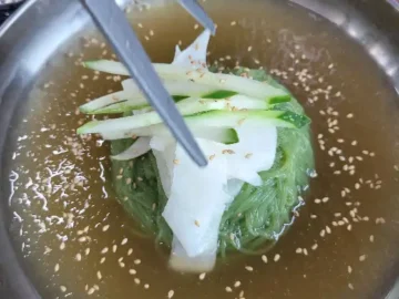 김이 모락모락 나는 뜨끈한 숯불고기와 함께 제공되는 시원한 육수의 물냉면