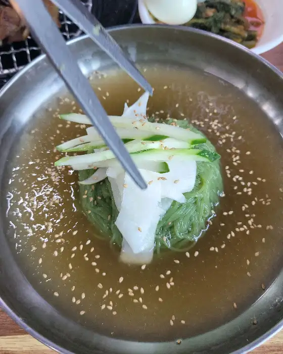 김이 모락모락 나는 뜨끈한 숯불고기와 함께 제공되는 시원한 육수의 물냉면