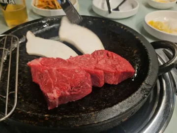 돌판 위에서 구워지고 있는 두툼한 한우 등심과 새송이버섯