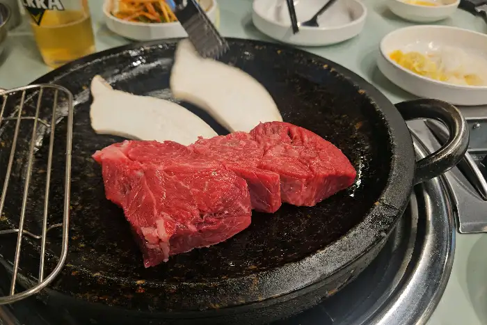 돌판 위에서 구워지고 있는 두툼한 한우 등심과 새송이버섯