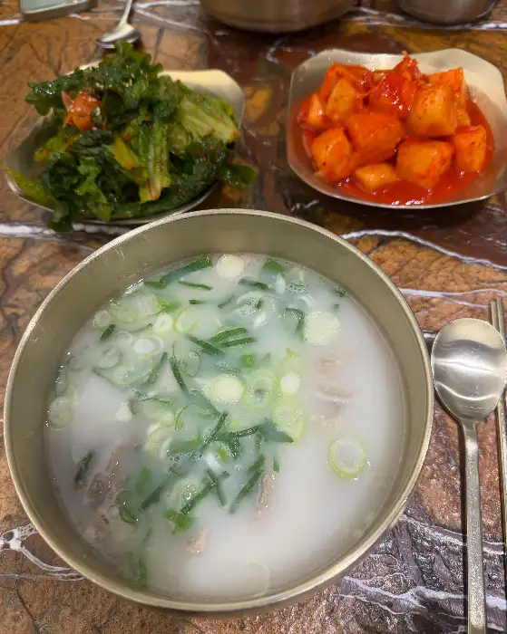 김치와 깍두기가 담긴 접시와 설렁탕이 놓여 있는 모습, 놋수저 세트가 함께 보인다.