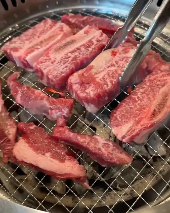 신선한 생갈비 여러 점이 불판 위에서 구워지고 있는 모습