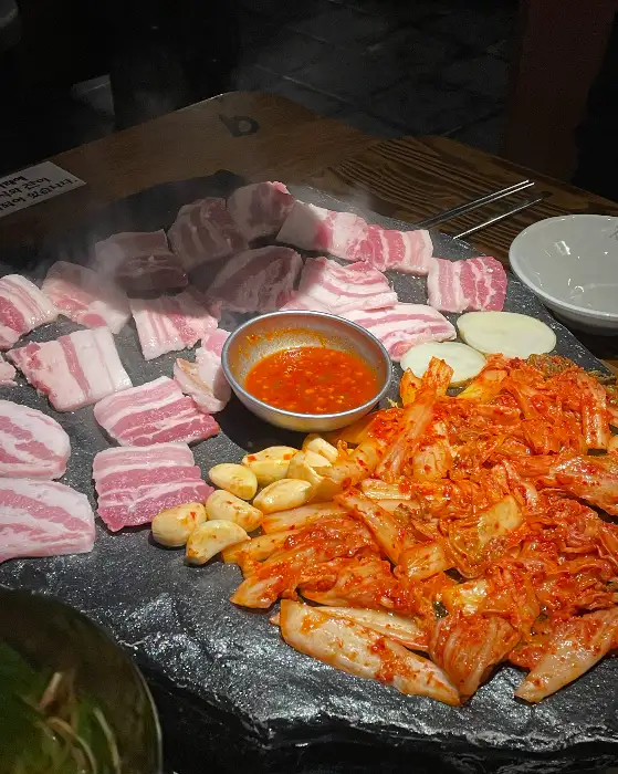 석암생소금구이 진주하대점 돌판에 구워지는 생고기와 김치, 마늘