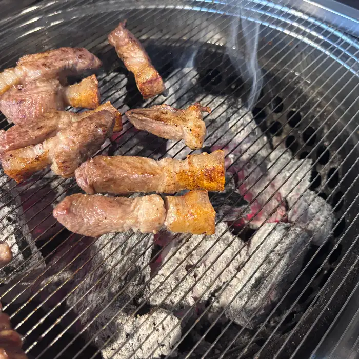 제주흑돈 본점의 숯불 위에서 구워지고 있는 흑돼지 조각들, 김이 모락모락 피어나고 있다