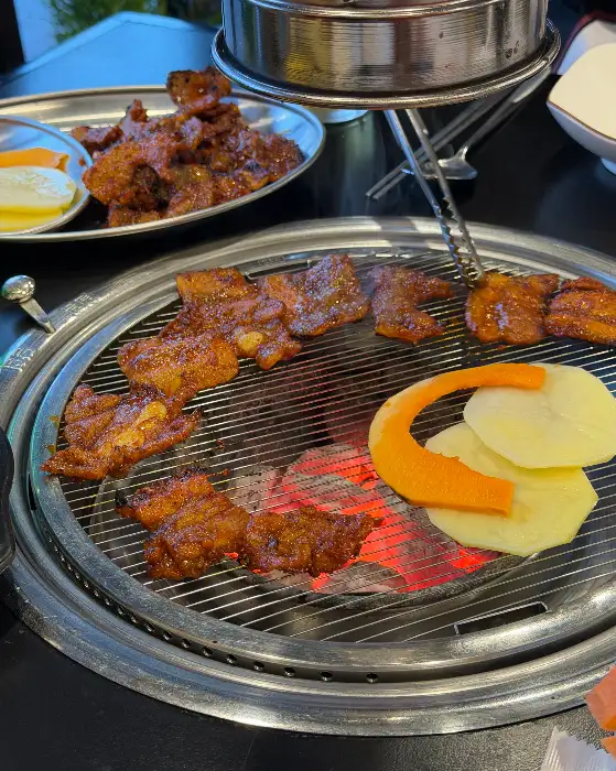 숯불 위에서 맛있게 익어가는 양념 돼지갈비와 얇게 썬 감자, 당근