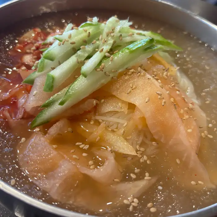 시원해 보이는 김치말이 국수 그릇, 고명으로 오이채와 깨가 뿌려져 있다