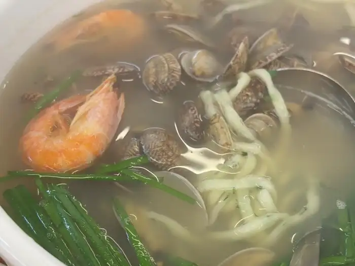 부추해물칼국수 그릇에 담긴 큼직한 새우와 조개, 그리고 푸릇한 부추가 돋보이는 모습