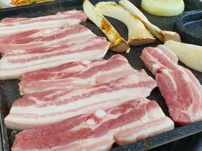 신선한 삼겹살이 먹음직스럽게 불판 위에 놓여 있는 모습